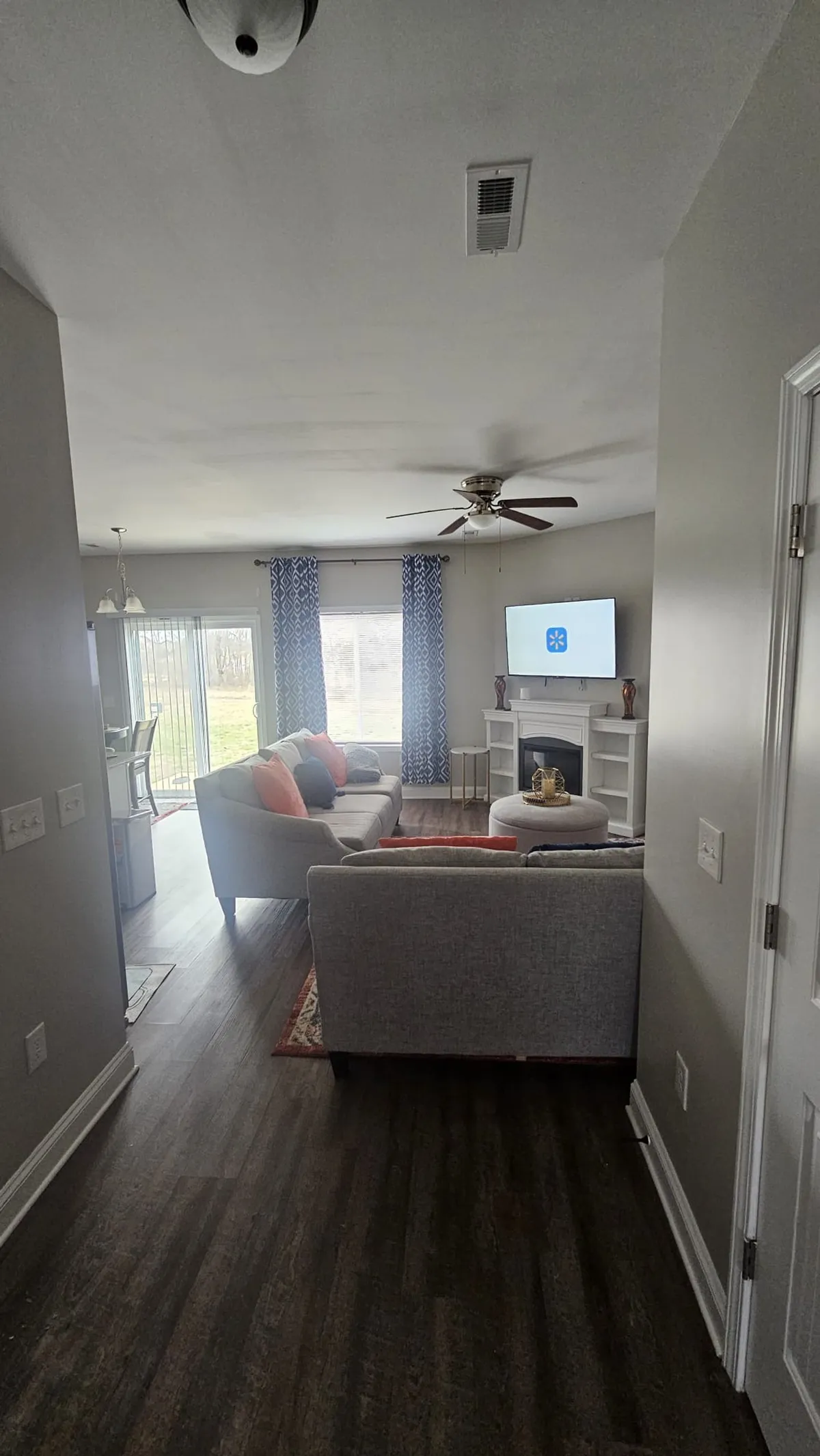 The image captures a bright and inviting living room featuring a plush sofa adorned with colorful pillows, a cozy fireplace, a mounted television, and a large window that floods the space with natural light. The room exudes a welcoming atmosphere, ideal for relaxing, watching TV, and spending time with loved ones.