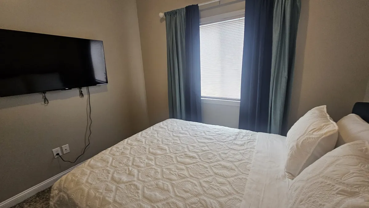 A cozy bedroom with a plush bed situated near a window, featuring curtains and a television across from the bed. The room exudes a welcoming, homey atmosphere perfect for relaxing after a day of exploring the city.