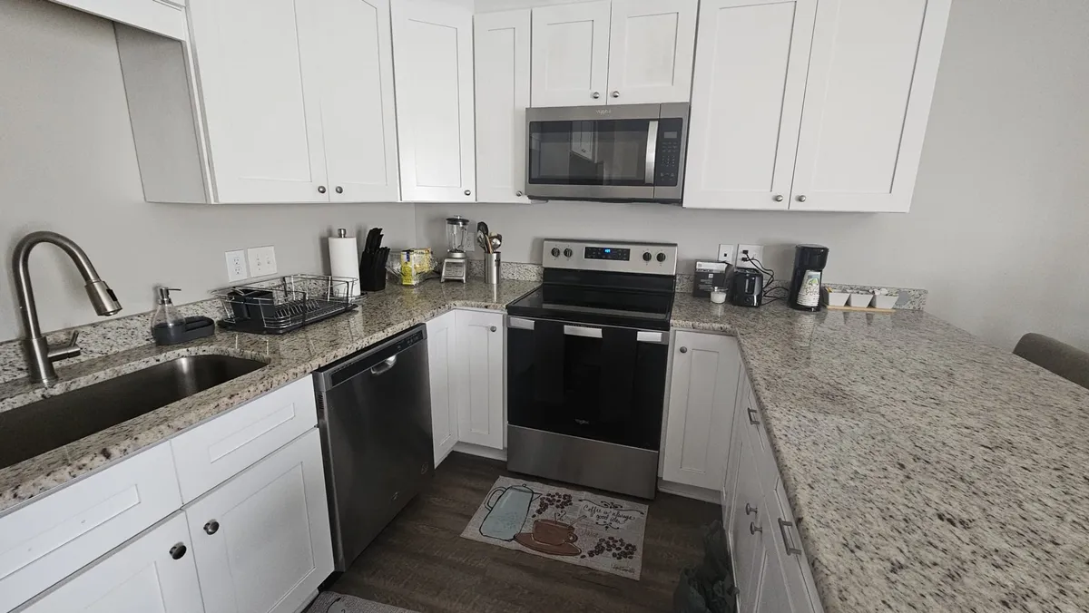 This image shows a cozy and modern kitchen with granite countertops, stainless steel appliances, a kitchen sink, and a dedicated coffee station. The setting is warm and welcoming, ideal for cooking, entertaining, and family gatherings.