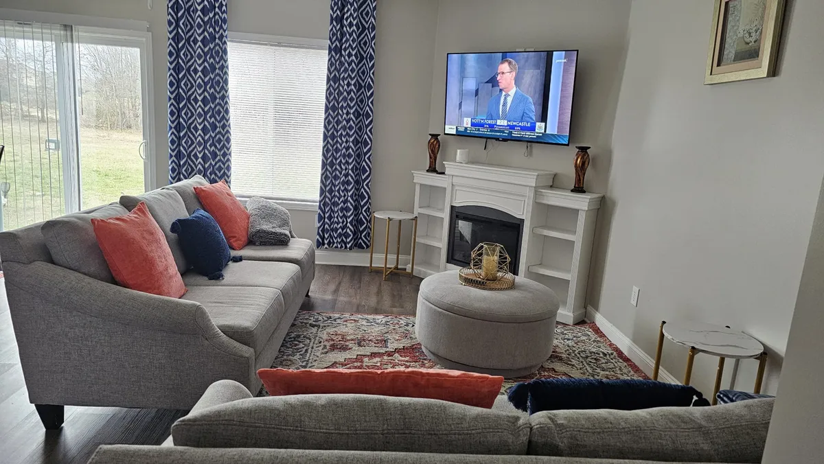 A cozy living room with a sofa, television, coffee table, and a welcoming fireplace. The space is well-lit and arranged for social gatherings or unwinding after a busy day at the track.
