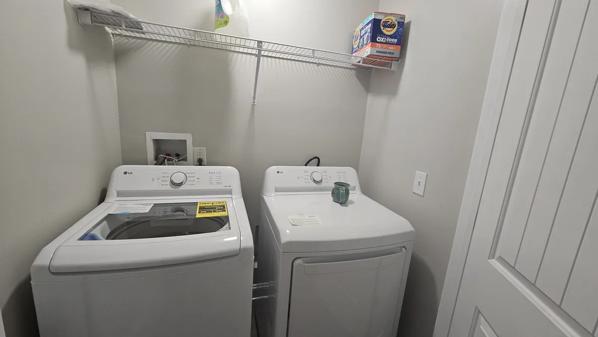 This image showcases a well-organized laundry area featuring a washing machine, dryer, and a shelf stocked with laundry supplies. The setting is neat and practical, conveying a sense of order and readiness for daily routines.